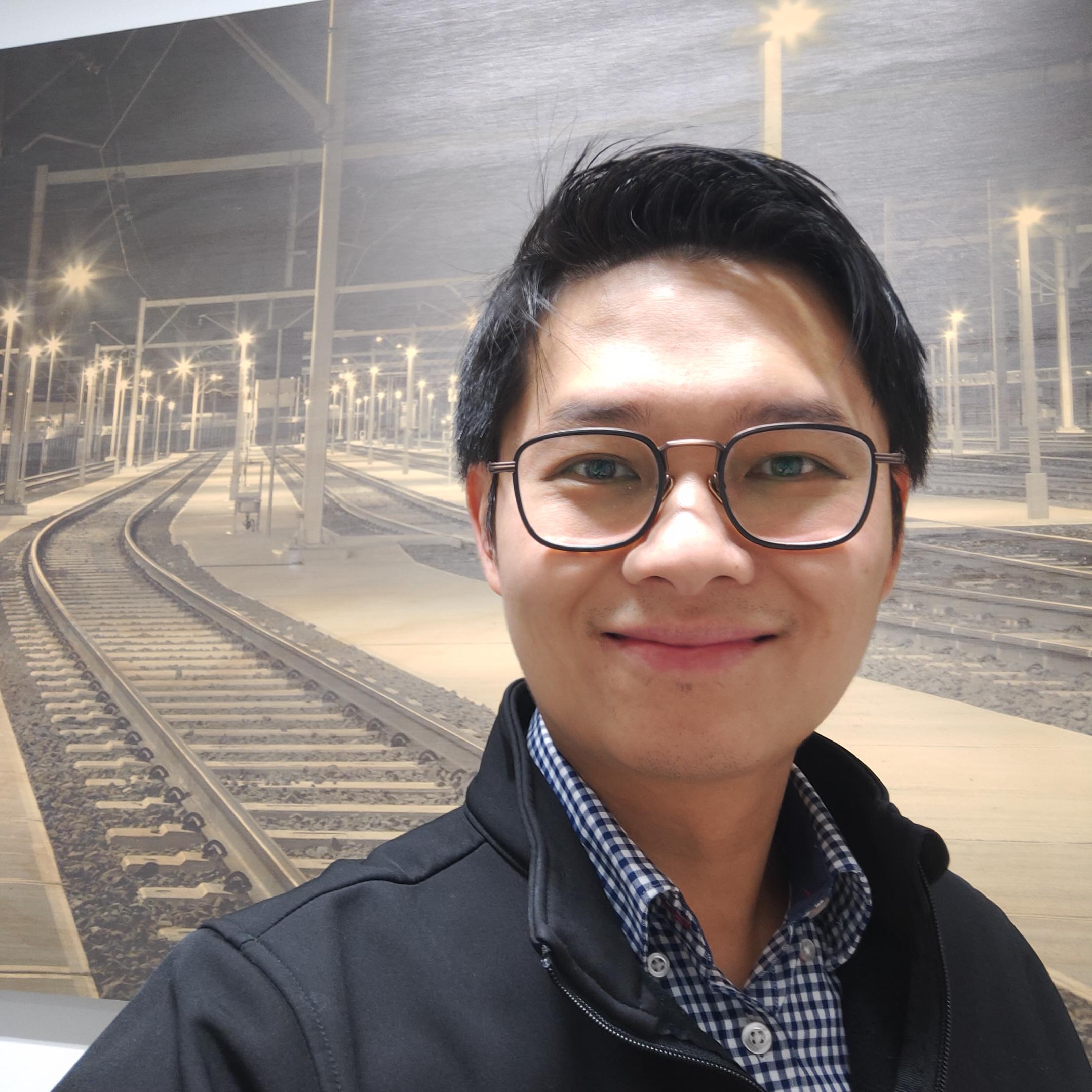 Man in glasses standing on a rail platform at night.