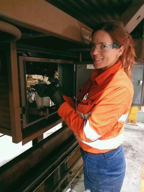 Female electrician working on the under-carriage of a train.