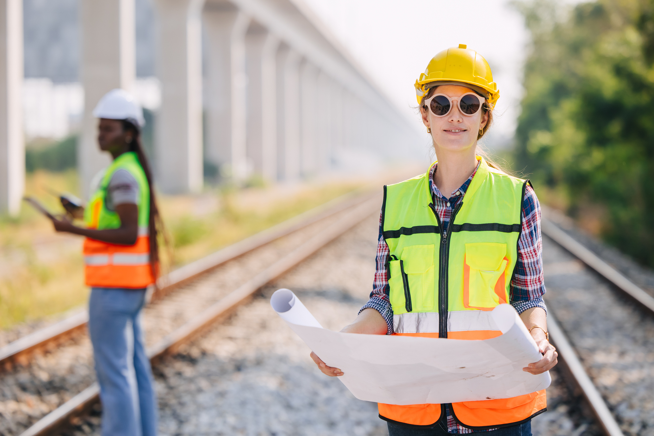 female rail worker looking at chart and standing near a rail line.