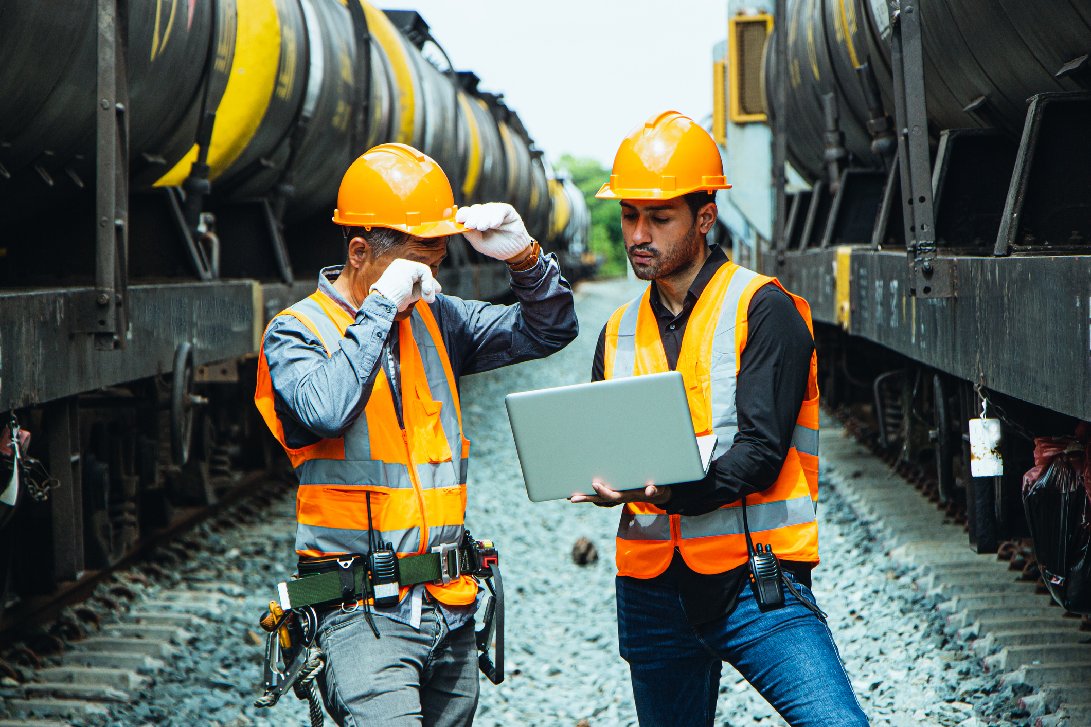 Engineer and rail worker with laptop standing alongside  rail wagons.