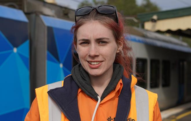 Female track work in high viz standing beside train at station.